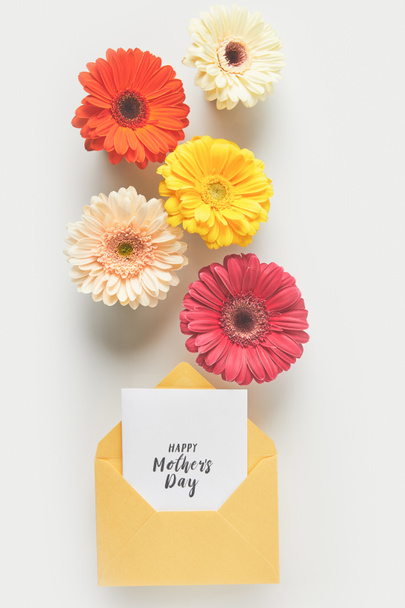 top view of beautiful tender gerbera flowers and envelope with happy mothers day greeting card on grey - Fotografie, Obrázek