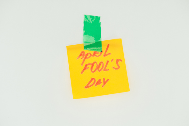 close up view of note with april fools day lettering and sticky tape isolated on grey, april fools day concept - Фото, изображение
