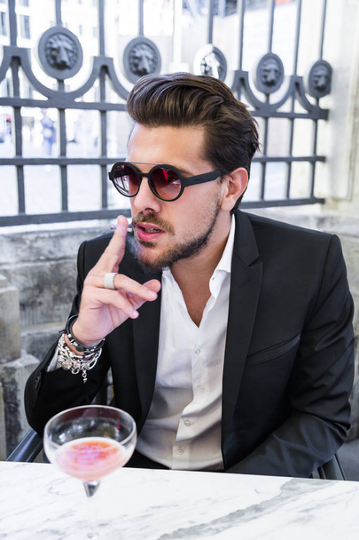 Male model in black suit sitting on chair and smoking cigarette - Photo, Image