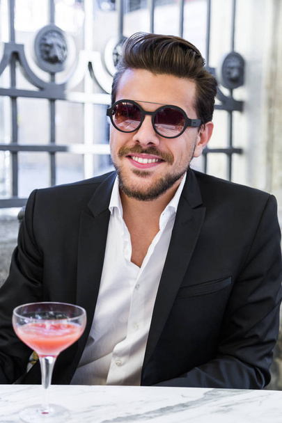 Man in black suit sitting on chair and drinking coctail - Foto, imagen