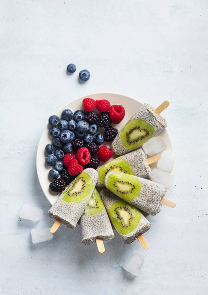 Kiwi Coconut Chia Popsicles and fresh ripe forest berries on the - Fotoğraf, Görsel