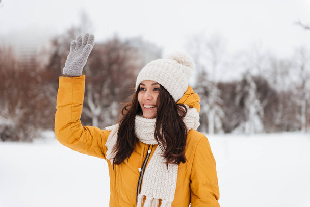 Young positive woman waving and greeting with somebody in snow park - Foto, Imagem