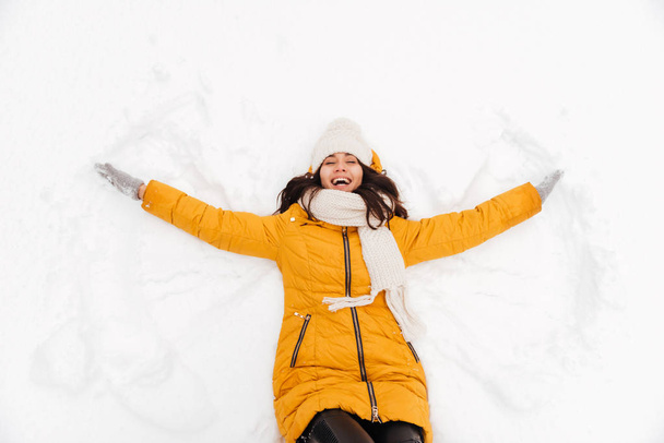 Happy playful lady lying on snow and making snow angel figure - Фото, изображение