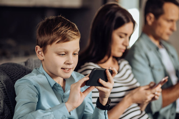 Pre-teen boy playing on phone next to his parents - Photo, image