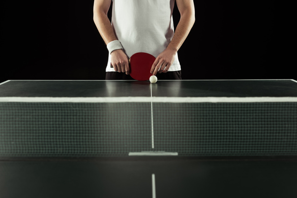 partial view of tennis player with racket standing at tennis table isolated on black - Фото, зображення