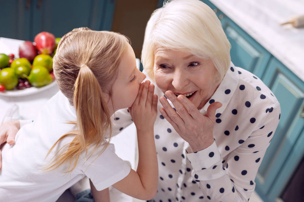 Cheerful girl and her grandmother sharing secrets - Fotoğraf, Görsel