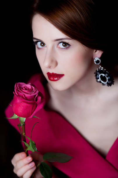 Young surprised woman in red Victorian epoch clothes with red rose on dark background - Photo, Image