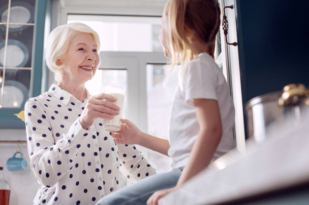 Caring senior woman giving a glass of milk to granddaughter - Valokuva, kuva