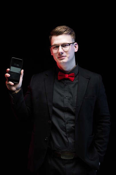 Tyylikäs blondi mies näyttää älypuhelimen mustalla taustalla
  - Valokuva, kuva