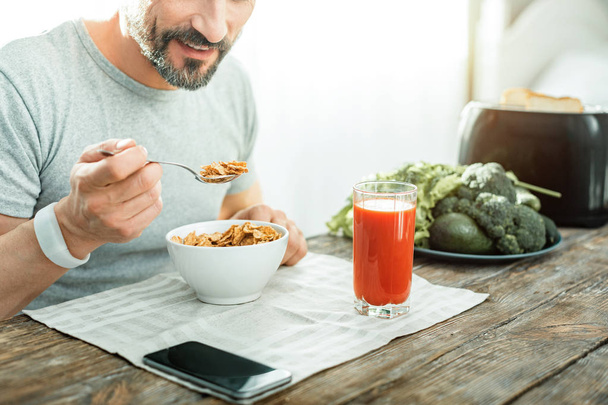 Satisfied unshaken man eating cereals and holding a spoon. - Fotó, kép