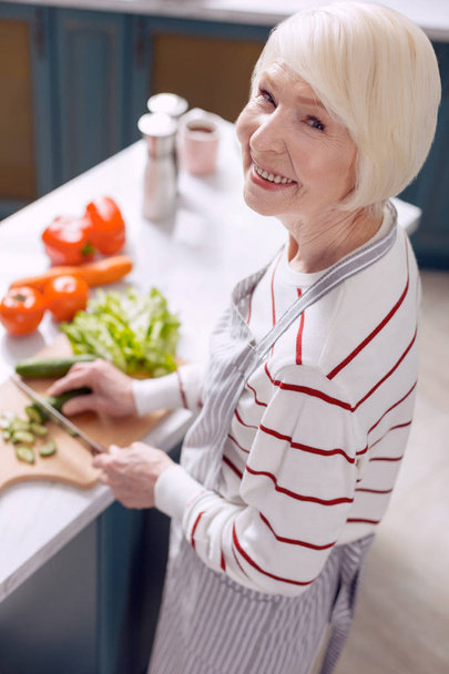 Cheerful senior lady posing while making salad - Фото, зображення