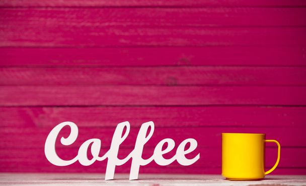 Wortkaffee und gelbe Tasse Kaffee auf rosa Holzgrund. Niedrige Sicht der Dinge  - Foto, Bild