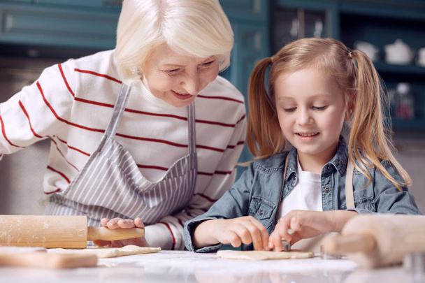 Grandmother watching granddaughter cut out cookies - Photo, Image