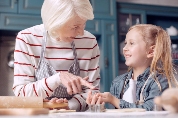 Pleasant woman pointing at cookie in her granddaughters hands - Foto, Imagem