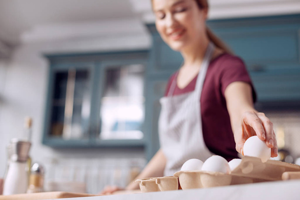 Pleasant young woman taking egg from egg carton - Foto, imagen