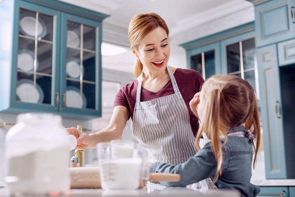 Cheerful woman wiping away flour from daughters forehead - Foto, Imagem