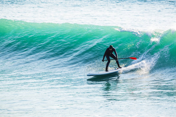 Surfer on stand up paddle board on blue wave. Winter surfing in ocean - Photo, Image