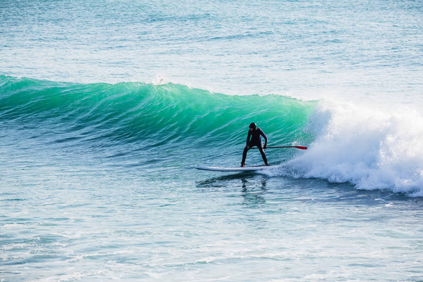 Surfeur debout planche à pagaie sur vague bleue. Surf d'hiver dans l'océan
 - Photo, image