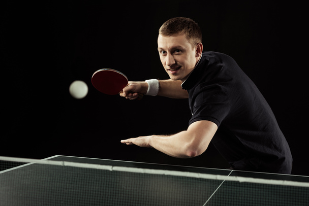 jogador de tênis sorridente em uniforme jogando tênis de mesa isolado em preto
 - Foto, Imagem