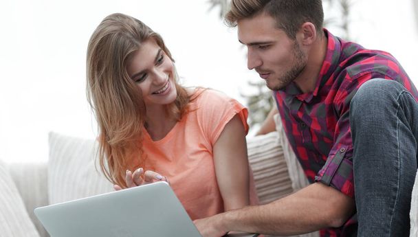 young couple is using a laptop and smiling while sitting on sofa at home - Foto, imagen