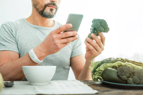 Occupied concentrated man holding a broccoli using his cellphone. - 写真・画像