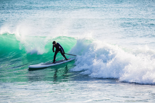 Surfer on stand up paddle board on blue wave. Winter surfing in ocean - Photo, image