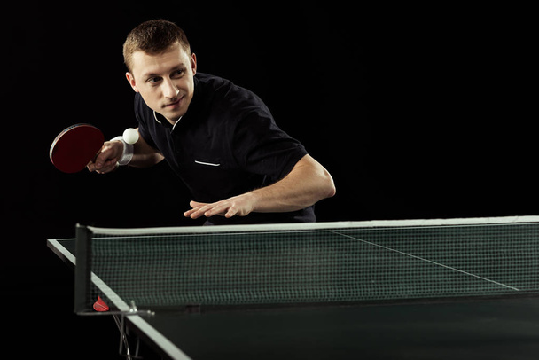 portrait of young tennis player in uniform playing table tennis isolated on black - Photo, Image