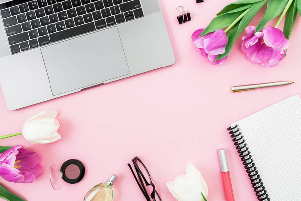 Bureau met laptop, witte tulpen, bril, pen en schaar op roze achtergrond. Flat lag. Bovenaanzicht. Freelancer samenstelling met kopie ruimte. - Foto, afbeelding
