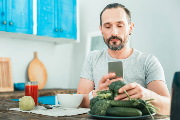 Calm pleasant man using his cellphone touching a broccoli. - Foto, afbeelding