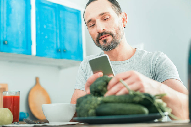 Satisfied smart man taking vegetables and using the cellphone. - Φωτογραφία, εικόνα