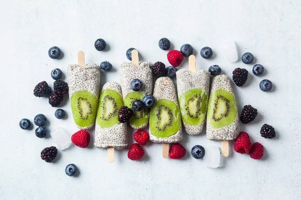 Kiwi Coconut Chia Popsicles and fresh ripe forest berries on the - Foto, afbeelding
