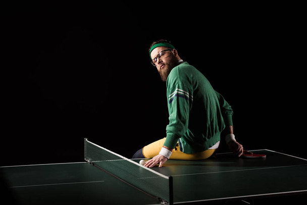 back view of bearded tennis player sitting on tennis table isolated on black - Fotografie, Obrázek