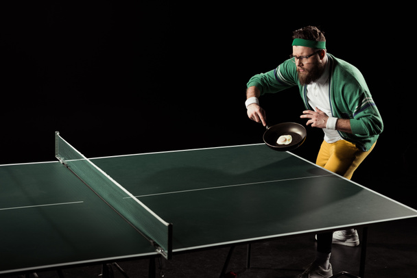 Tennisspieler mit Bratpfanne mit Ei Tischtennis spielen isoliert auf schwarz - Foto, Bild