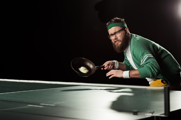 tennis player with frying pan with egg playing table tennis isolated on black - Φωτογραφία, εικόνα