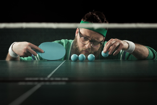бородатий тенісист дивиться на блакитні тенісні м'ячі на столі ізольовані на чорному
 - Фото, зображення