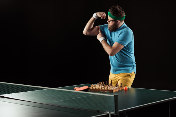 tennis player showing muscles while standing at tennis table with chess board isolated on black - 写真・画像