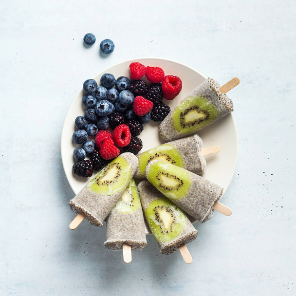 Kiwi Coconut Chia Popsicles and fresh ripe forest berries on the - Foto, imagen