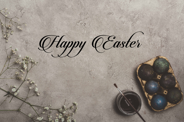 vista superior de huevos de Pascua pintados en bandeja con flores, pintura y pincel sobre hormigón con letras de Feliz Pascua
 - Foto, imagen
