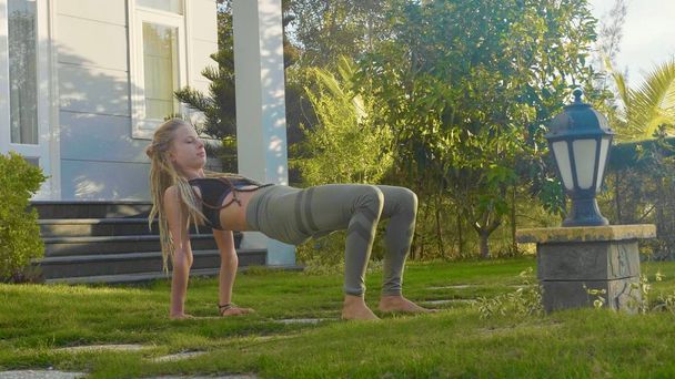 professionelle Vorstellung von Asana Yoga durch ein junges Mädchen im Hinterhof ihres Hauses - Foto, Bild