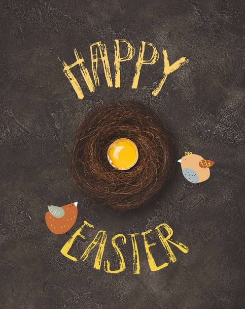 Draufsicht auf zerbrochenes Ei mit Eigelb im Nest auf Betonoberfläche mit Vögeln und frohem Osteraufdruck - Foto, Bild