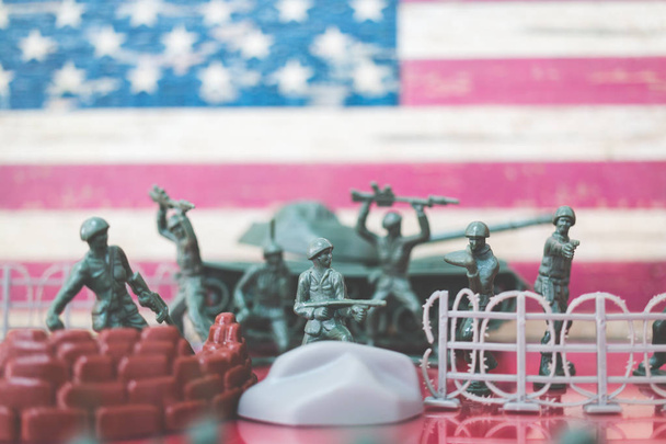 Soldados de brinquedo em miniatura em cena de batalha com fundo de bandeira americana
 - Foto, Imagem