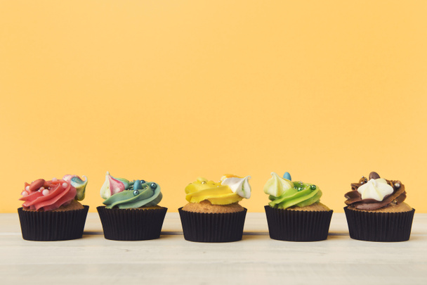 Schokoladen-Cupcakes in einer Reihe mit buntem Zuckerguss - Foto, Bild