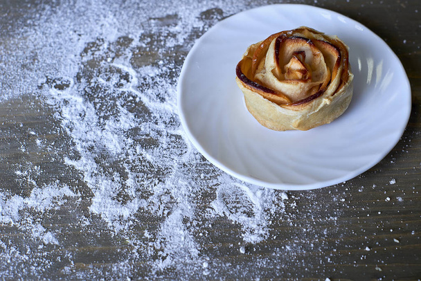 Смачна та солодка запечена випічка у формі троянди з яблучною начинкою на білій тарілці на дерев'яному фоні з касторовим цукром
 - Фото, зображення