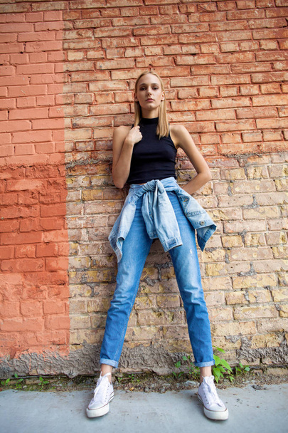 fashion girl standing near brick wall in denim and sneakers. Vogue Style - 写真・画像