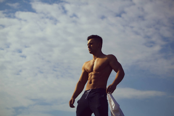 Sexy muscular man undressing on sky background - 写真・画像