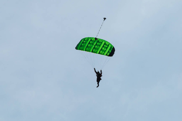 Fallschirmspringer mit grünem Fallschirm gegen strahlend blauen Himmel - Foto, Bild