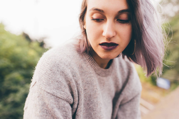 Muotokuva nuori valkoihoinen violetti harmaat hiukset nainen ulkona kaupungissa etsii yli, hymyillen
  - Valokuva, kuva