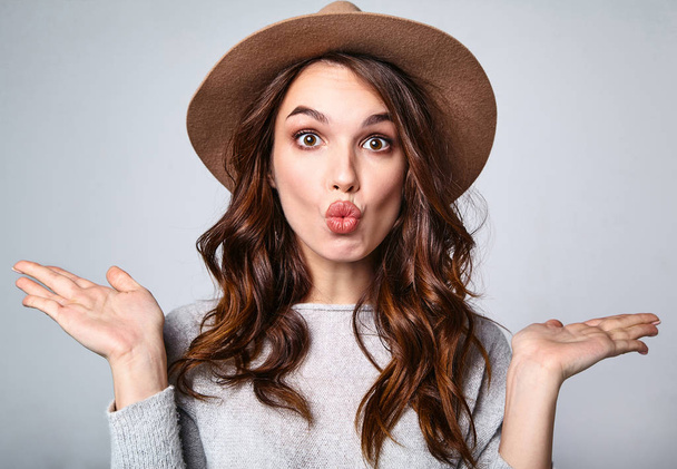 Portrait of young stylish laughing girl model in gray casual summer clothes in brown hat with natural makeup isolated on gray background. Looking at camera and giving air kiss - Foto, immagini