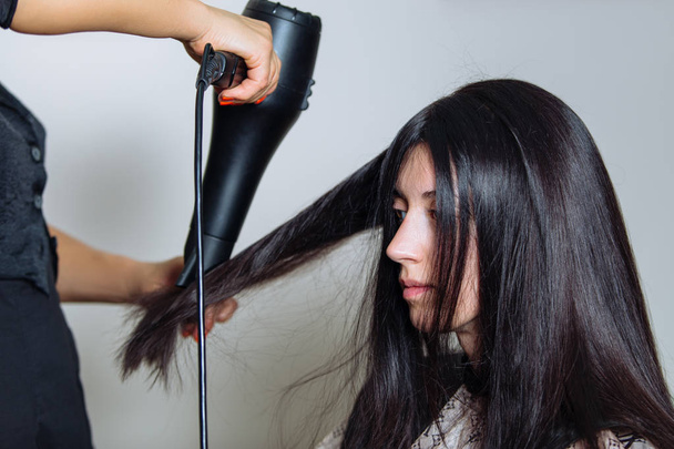 professioneller Friseur mit Haartrockner und Kamm am Haar des Kunden. - Foto, Bild