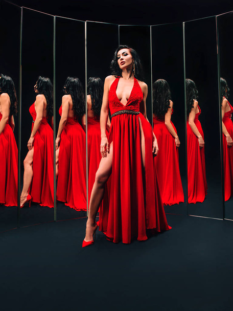 Portrait of beautiful brunette woman in red shoes and dress standing near the mirrors - Photo, Image